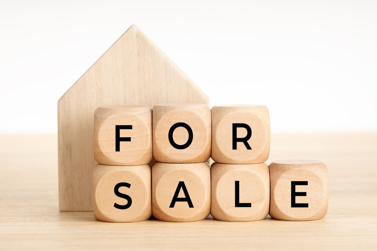 Plain wooden letter blocks that spell out βFOR SALEβ in front of an unadorned wooden house figure