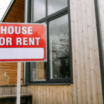 A “For Rent” sign displayed outside a wooden house