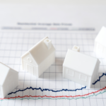 Four small white plastic house figures atop a real estate market growth chart