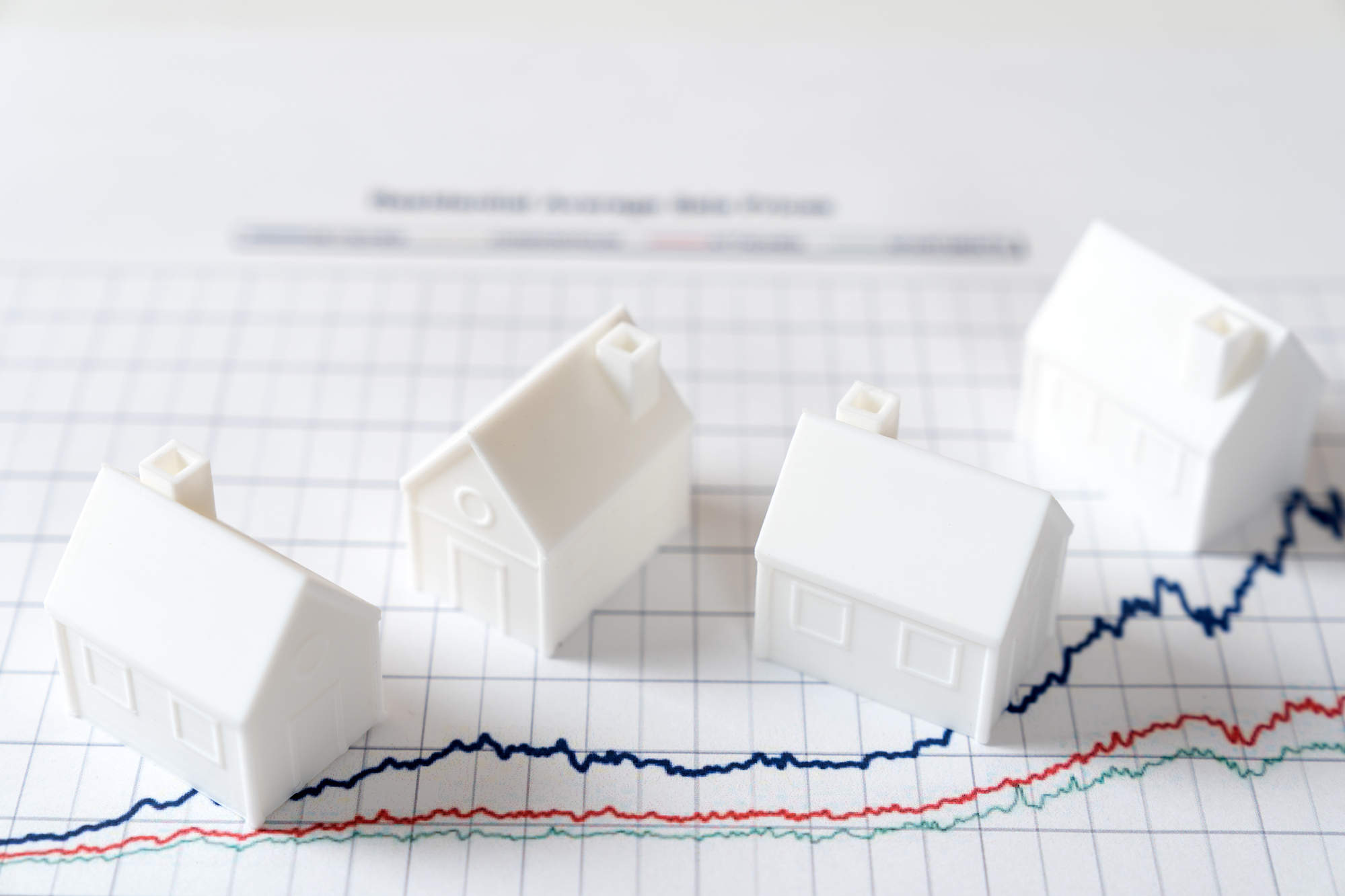Four small white plastic house figures atop a real estate market growth chart