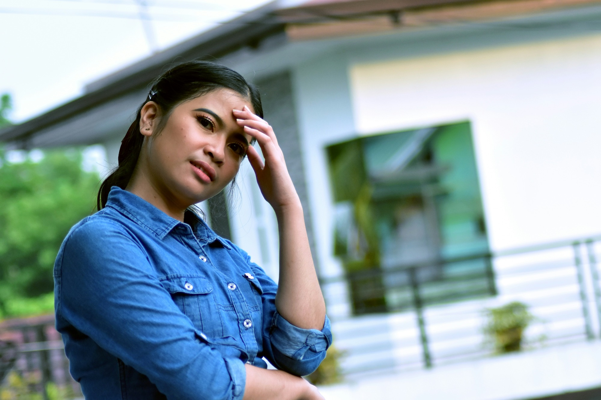 A woman stands in front of her house with her hand on her head