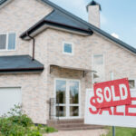 A “For Sale” sign in front of a house is covered up by a sign saying “Sold”