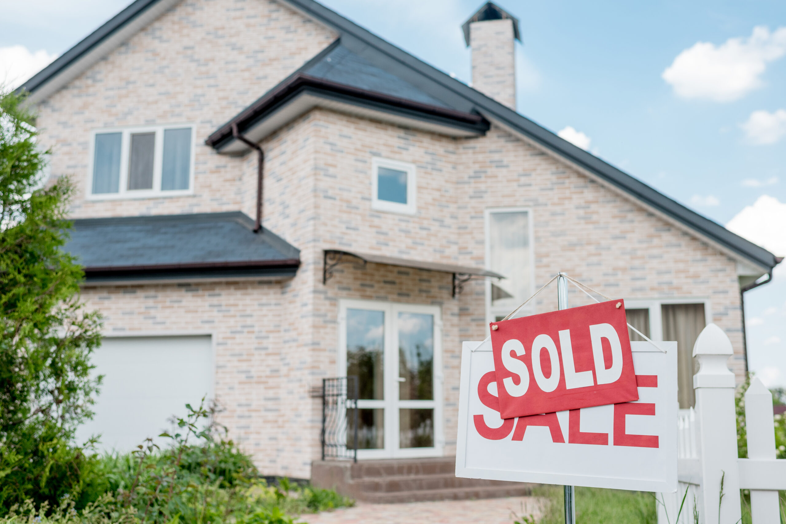 A “For Sale” sign in front of a house is covered up by a sign saying “Sold”