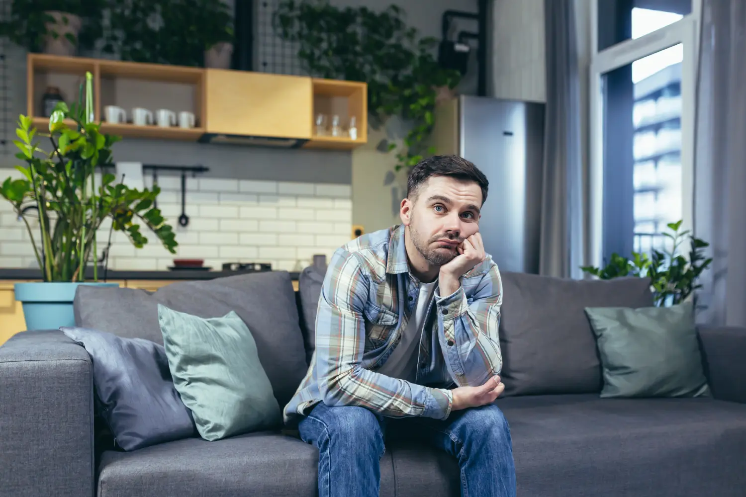 A pensive man sits on the sofa, resting his face on his hand