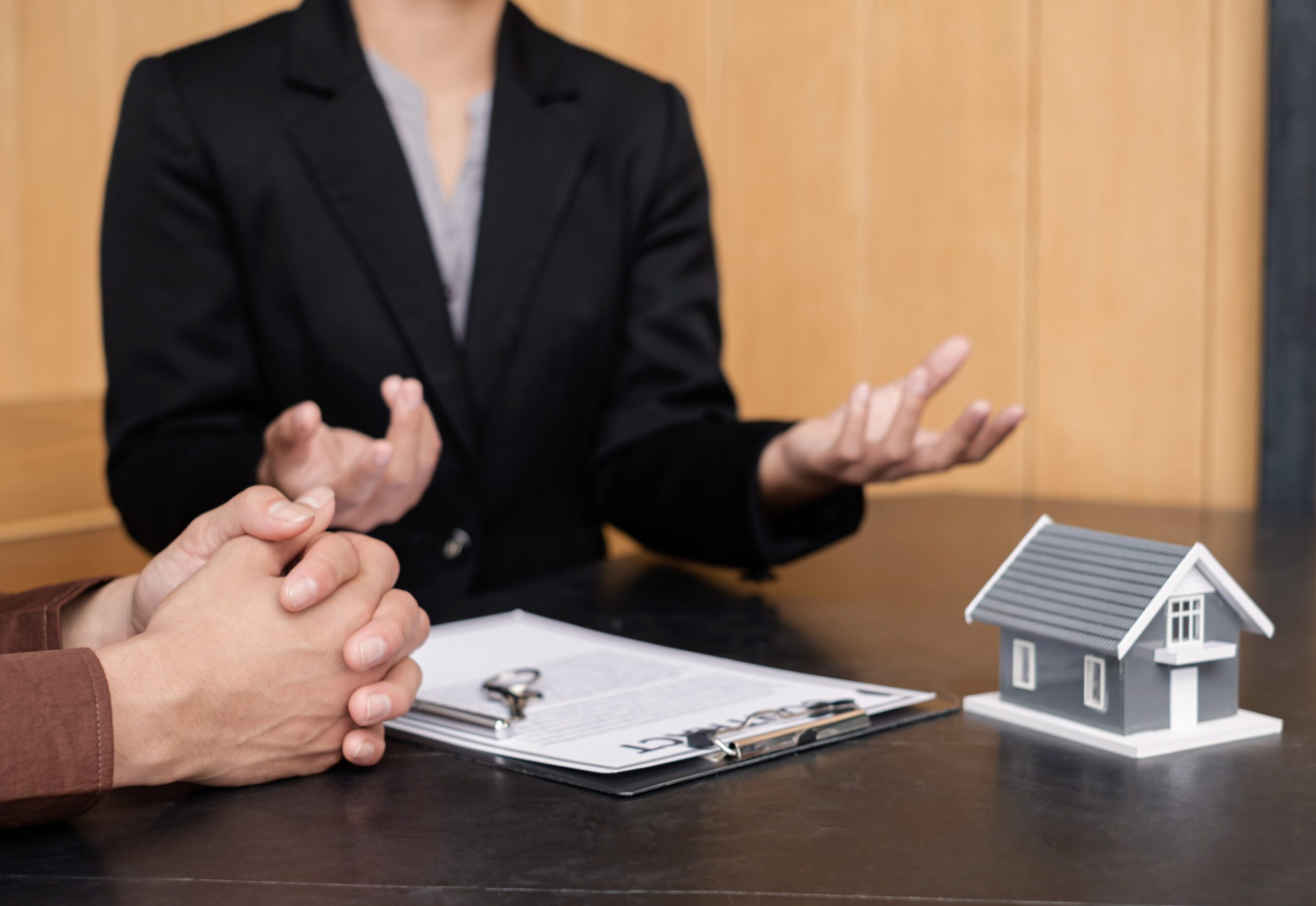 A real estate agent with a clipboard and model home explaining listing details to a seller