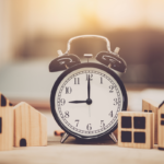 An alarm clock between two sets of wooden house figures