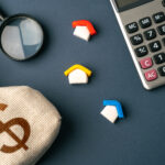 House figurines, a calculator, a money bag, and a magnifying glass on a dark background