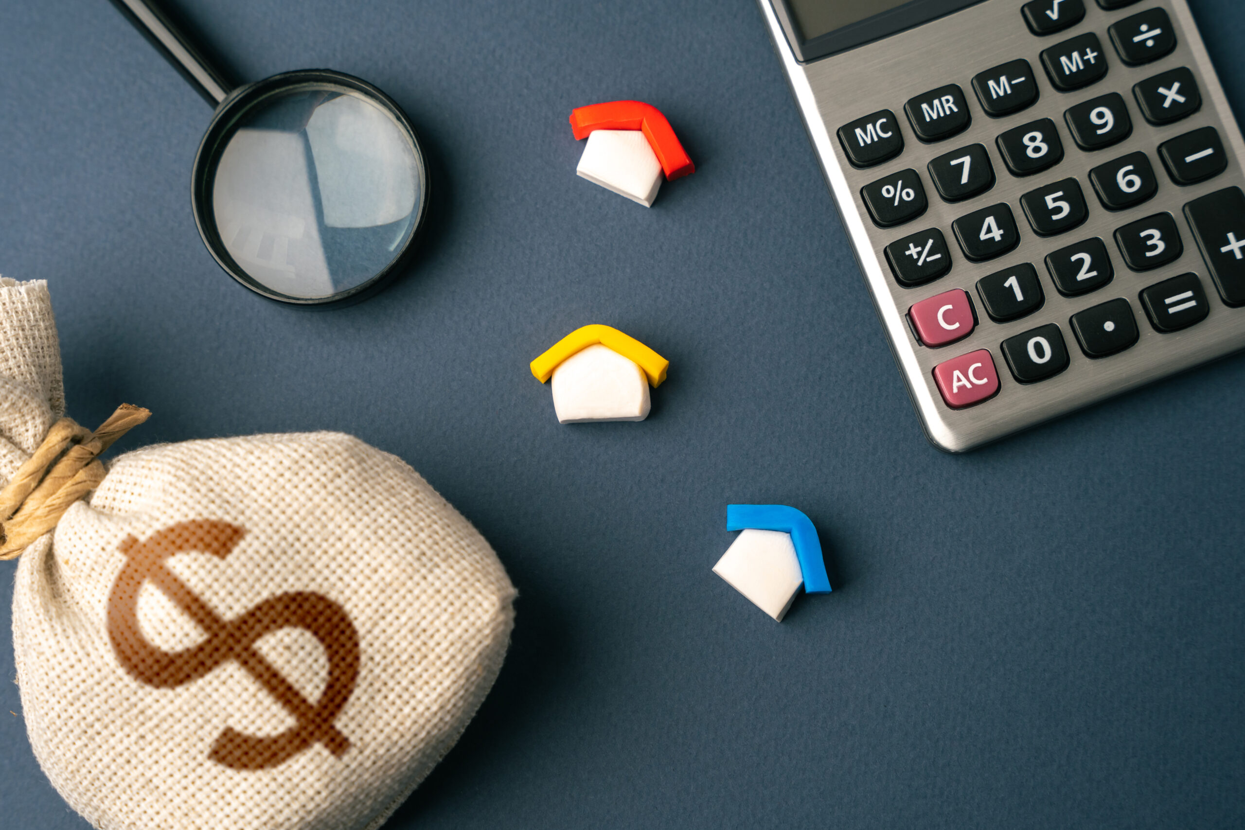 House figurines, a calculator, a money bag, and a magnifying glass on a dark background
