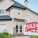 A “For Sale” sign in front of a house is covered up by a sign saying “Sold”