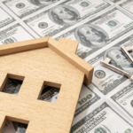 A flat wooden house figure and keys atop a background of continuous $100 bills