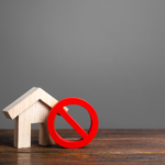 A red prohibited symbol against a wooden house figure