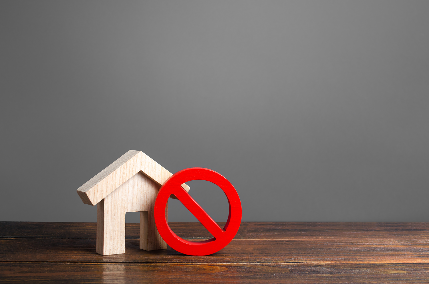 A red prohibited symbol against a wooden house figure