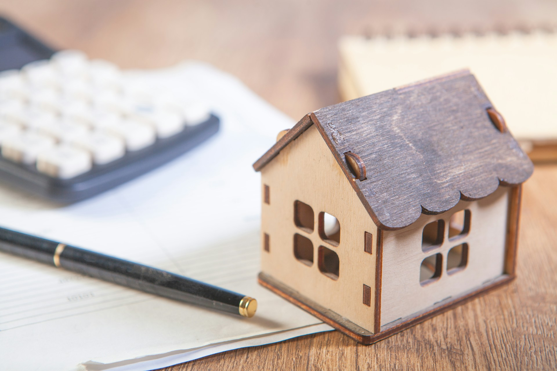 A close-up image of a miniature house, calculator, pen and paper