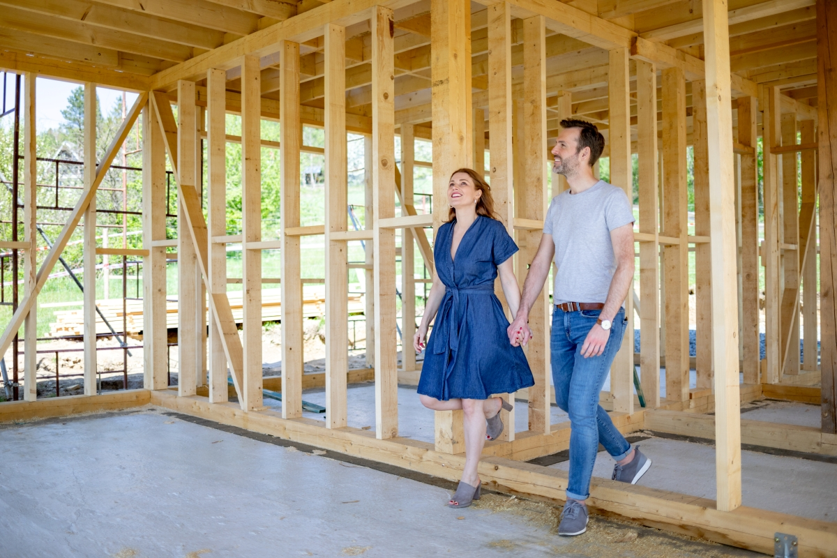 A happy couple holding hands walks through the wood frame of their new construction home