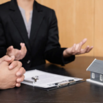 A real estate agent with a clipboard and model home explaining listing details to a seller