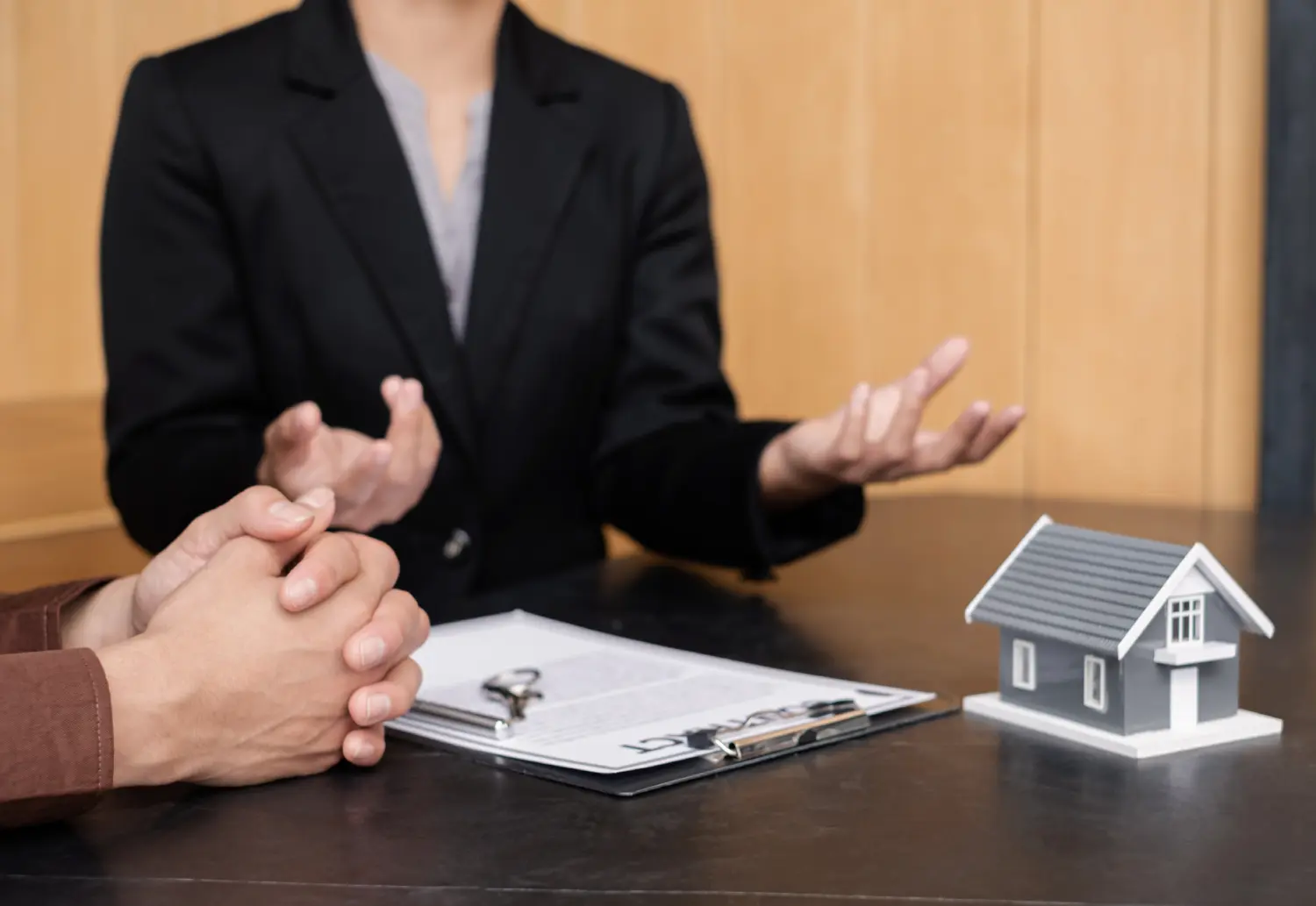 A real estate agent with a clipboard and model home explaining listing details to a seller